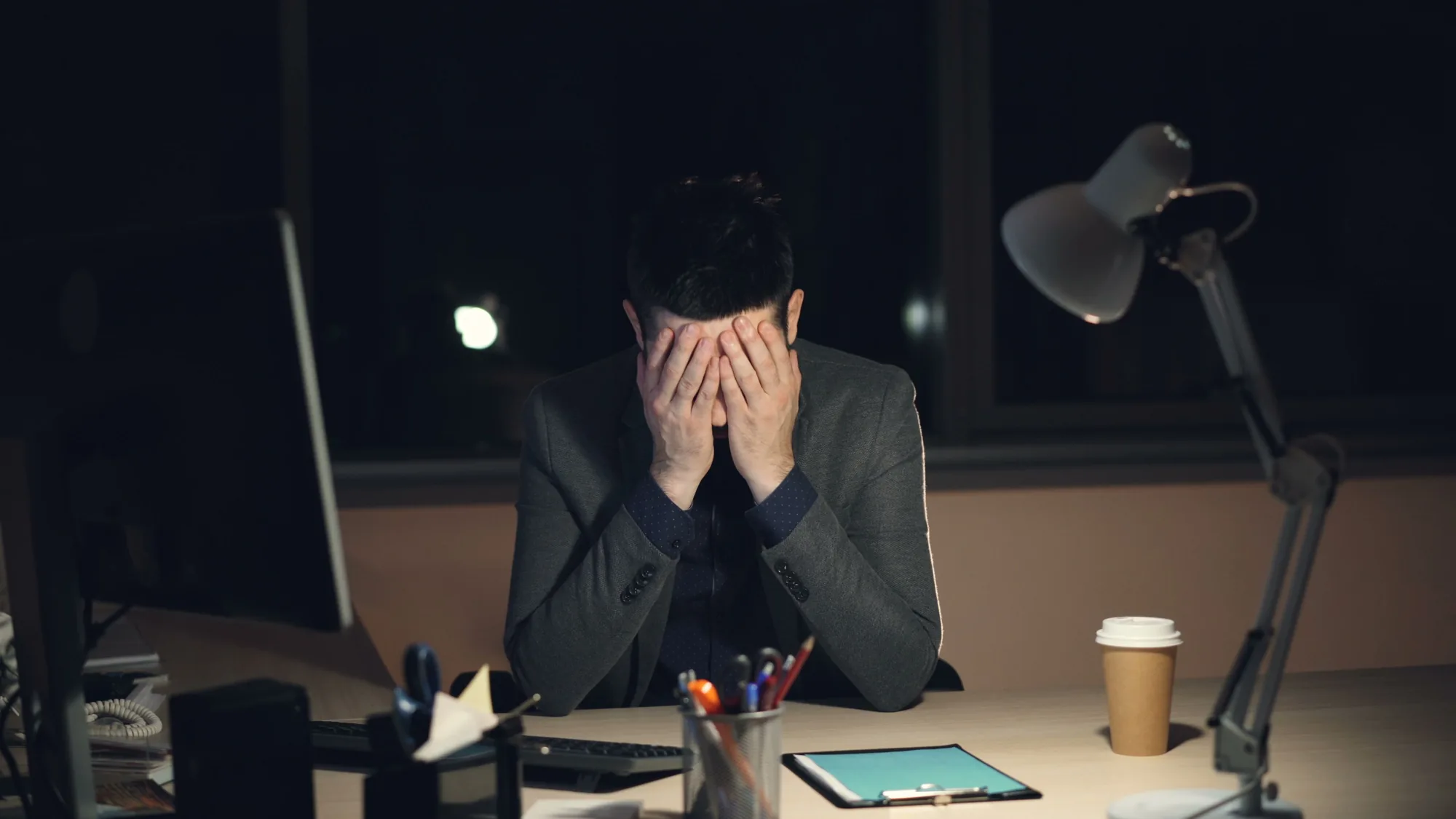 A tired professional at a desk covering his face while working late at a computer, illustrating AI review fatigue.