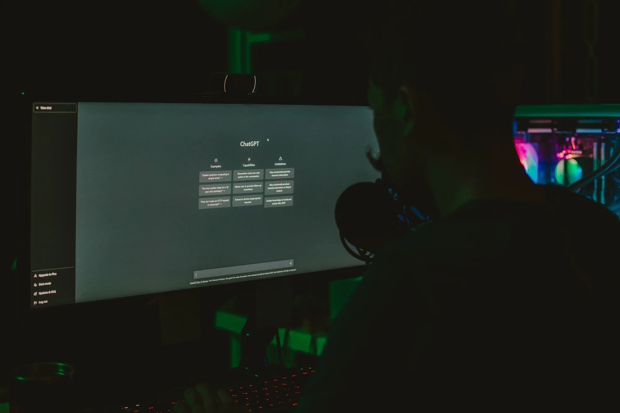 A developer working at a dark desk with multiple screens and an AI chat interface open.