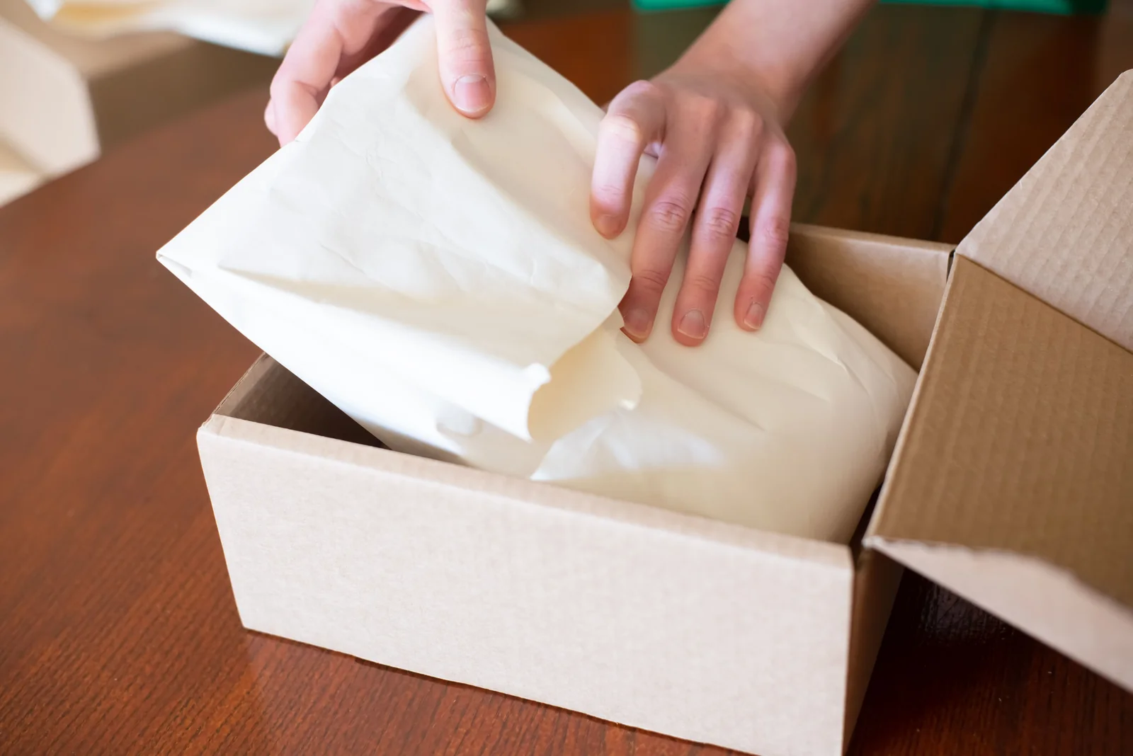 Hands wrapping merchandise inside a cardboard box while preparing an online order for shipping.