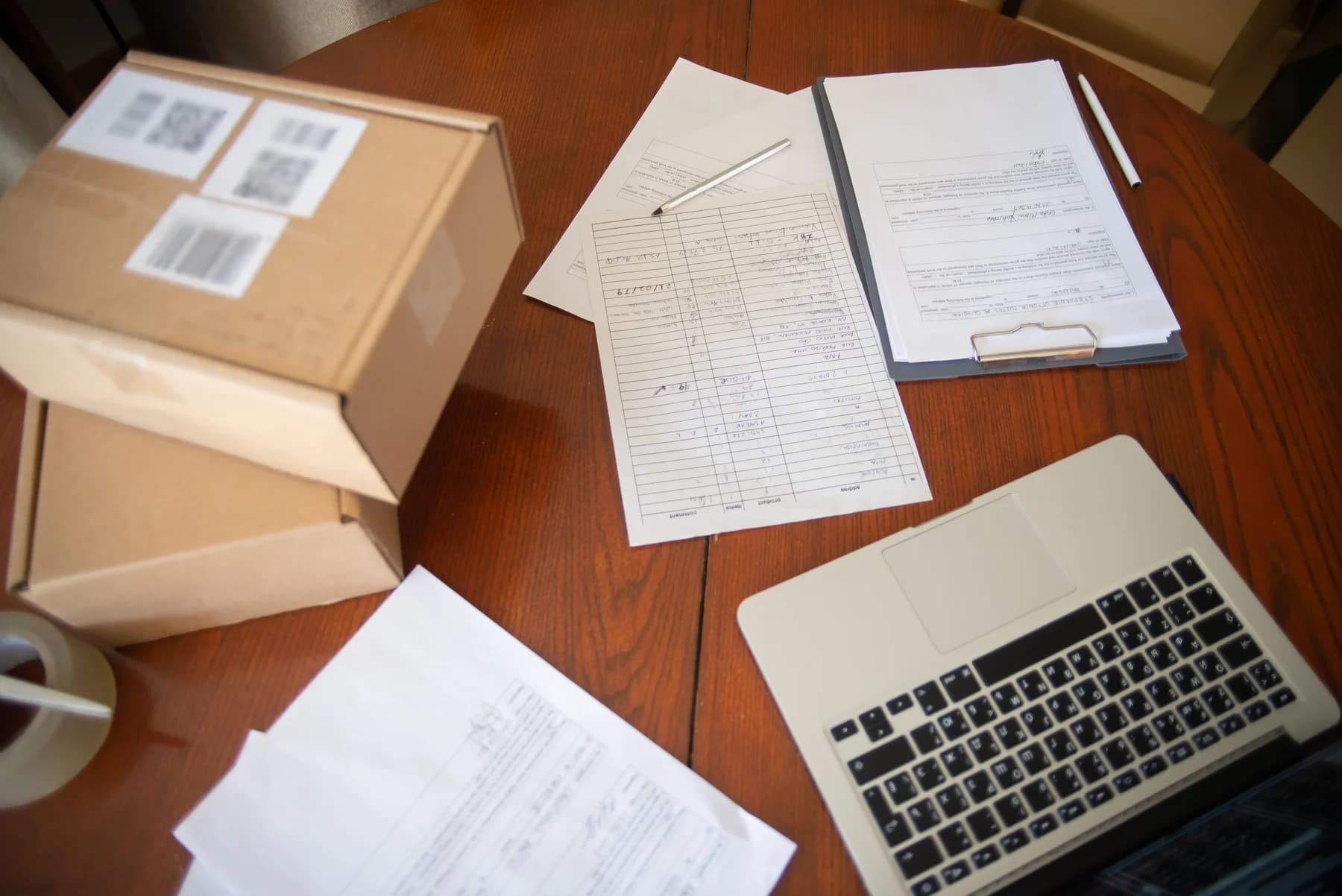 Laptop, shipping boxes, and order paperwork arranged on a wooden desk.