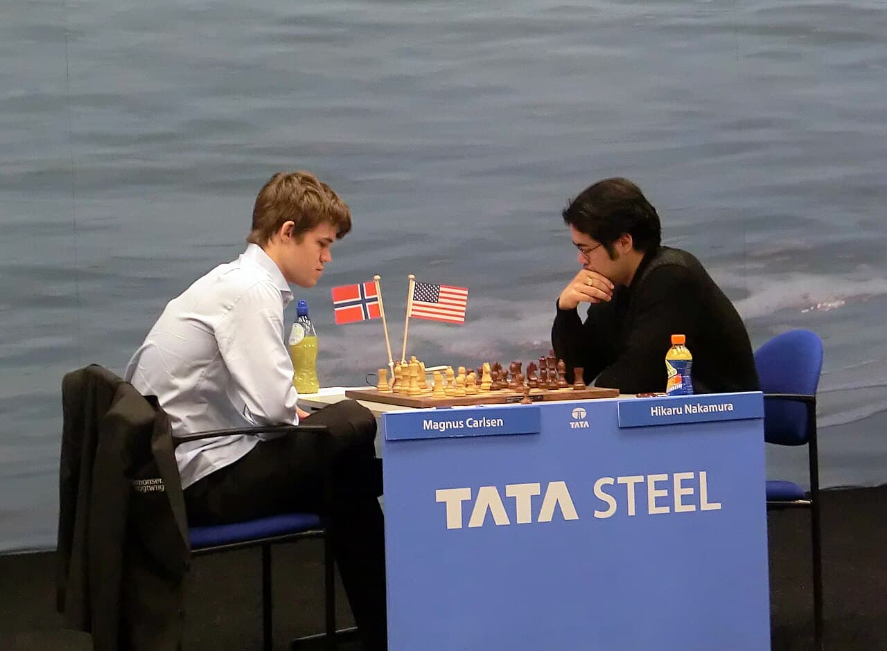Magnus Carlsen and Hikaru Nakamura facing each other across a chess board at the Tata Steel chess tournament in 2013.