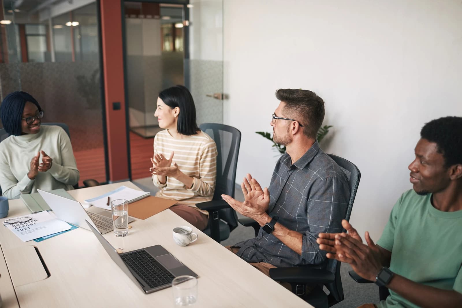 Four colleagues sit around a meeting table with laptops and applaud.
