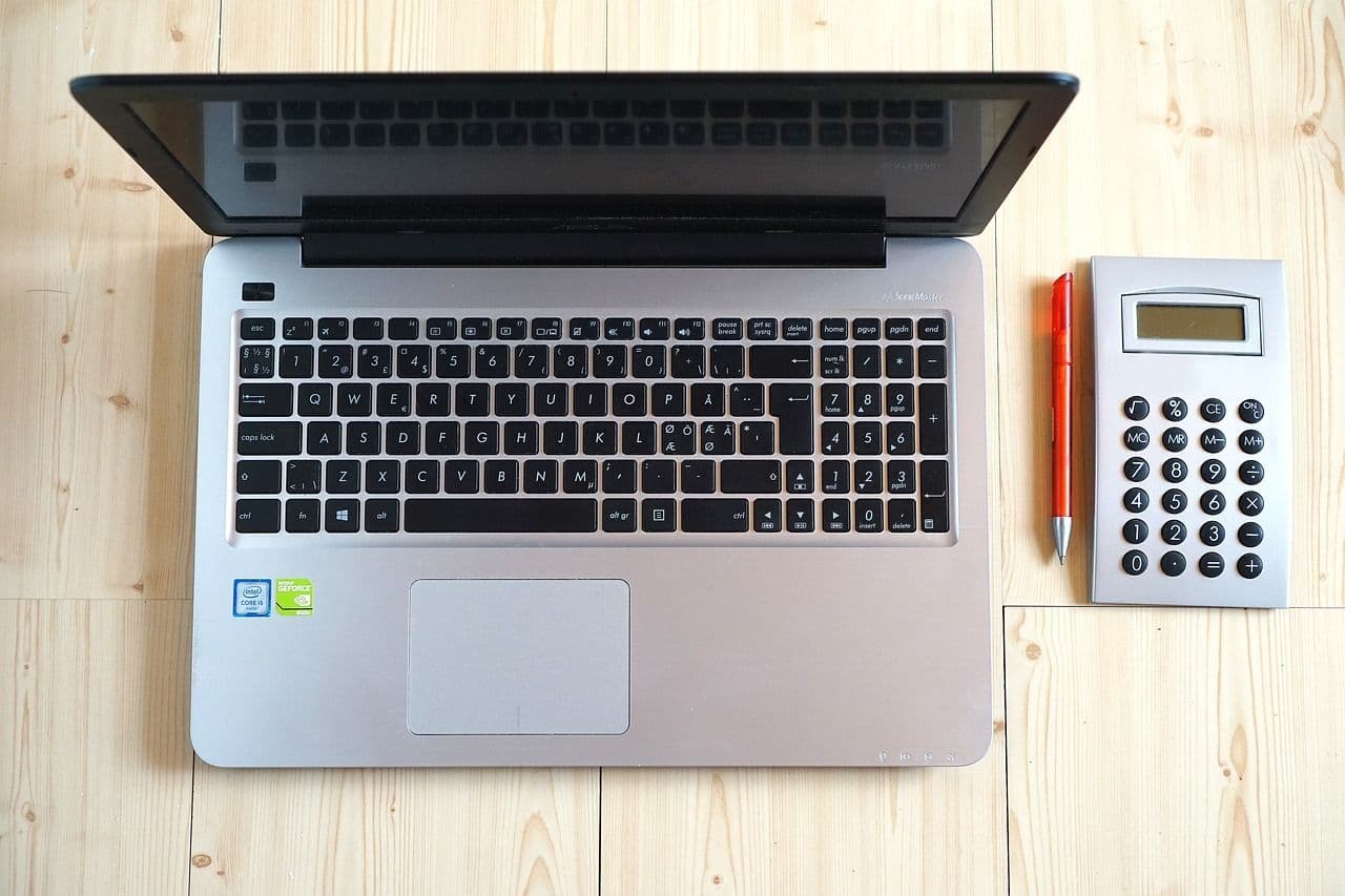 Laptop, calculator, notebook, and pen arranged on an office desk for planning a website budget.