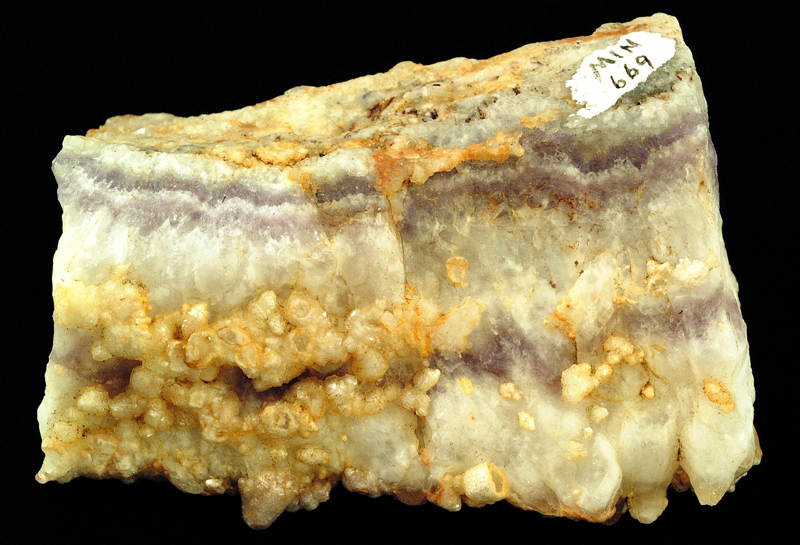 Quartz specimen composed of silicon dioxide, or SiO2, showing white and purple banded mineral material and quartz crystals.